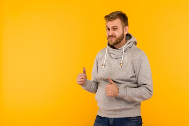 Bel homme européen attrayant en sweat à capuche gris pouce vers le haut sur l'image de fond jaune