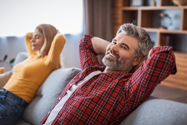 Un bel homme et une femme européens d'âge moyen et joyeux profitent du repos et de la détente en rêvant sur un canapé