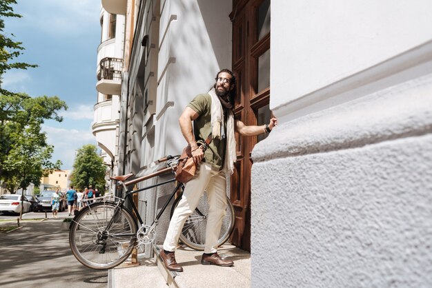 Bel homme gentil regardant la rue tout en ouvrant la porte de sa maison