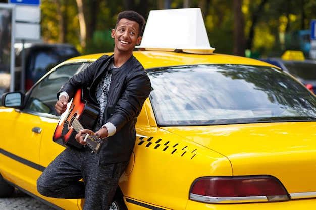 Bel homme avec guitare près de taxi jaune