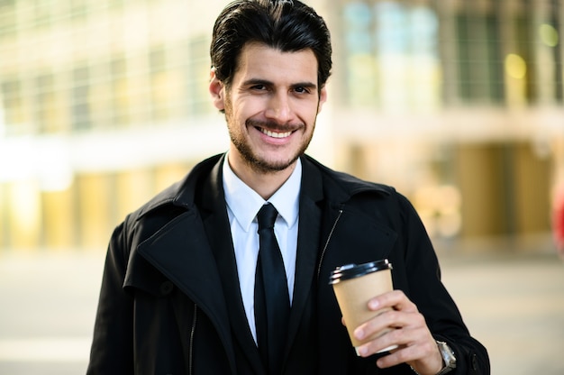 Bel homme habillé élégant tenant une tasse de café en plein air