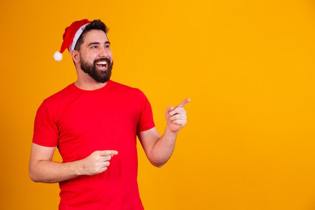 Bel homme habillé pour Noël portant un chapeau de père Noël pointant vers un espace de texte libre. promotion de fin d'année