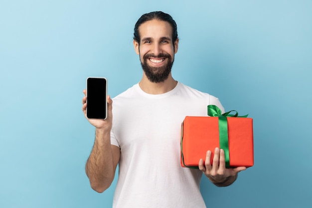 Bel homme heureux tenant une boîte-cadeau et un téléphone portable avec une maquette d'affichage vierge pour la publicité