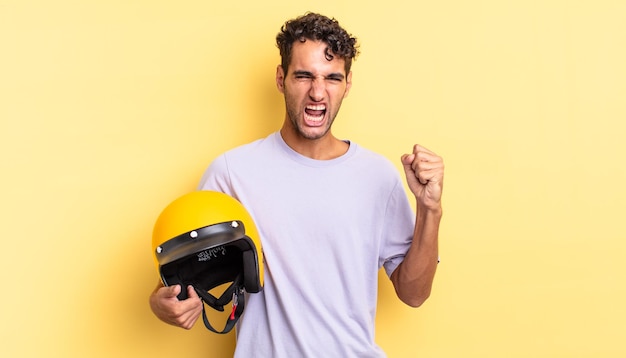 Bel homme hispanique criant agressivement avec une expression de colère. concept de casque de moto