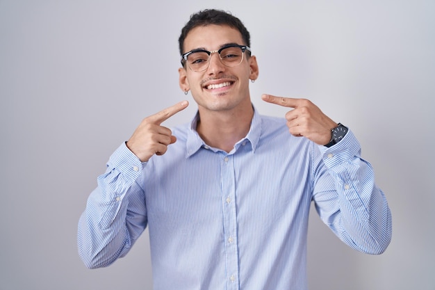 Bel homme hispanique portant des vêtements d'affaires et des lunettes souriant joyeux montrant et pointant avec les doigts les dents et la bouche. concept de santé dentaire.