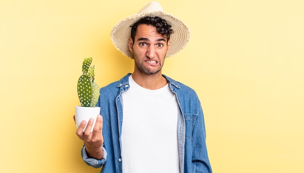 Bel homme hispanique à la recherche de concept d'agriculteur et de cactus perplexe et confus