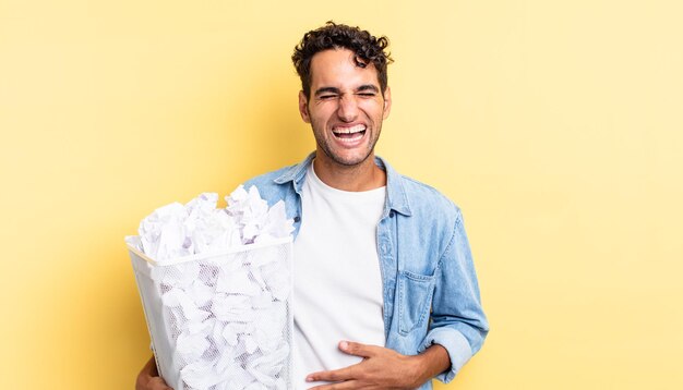 Bel homme hispanique riant aux éclats d'une blague hilarante. concept de poubelle de boules de papier