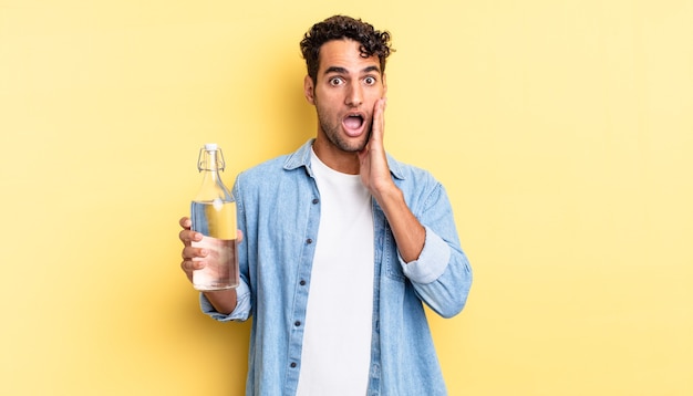 Bel homme hispanique se sentant choqué et effrayé. concept de bouteille d'eau