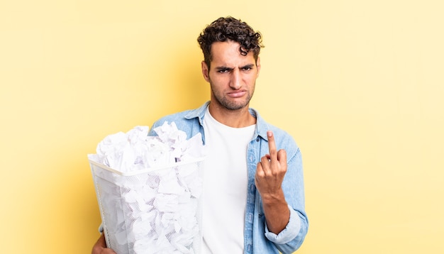 Bel homme hispanique se sentant en colère, agacé, rebelle et agressif. concept de poubelle de boules de papier