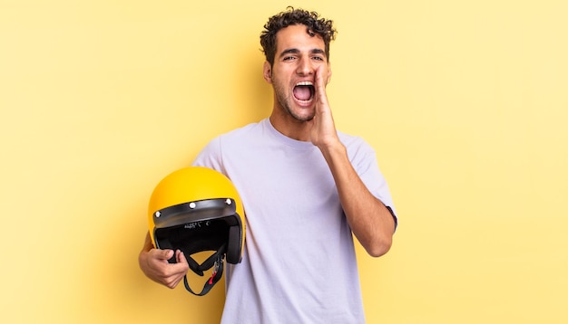 Bel homme hispanique se sentant heureux, donnant un grand cri avec les mains à côté de la bouche. concept de casque de moto