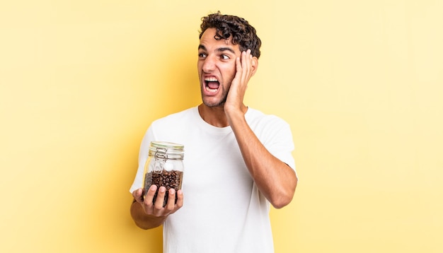 Bel homme hispanique se sentant heureux, excité et surpris. bouteille de grains de café