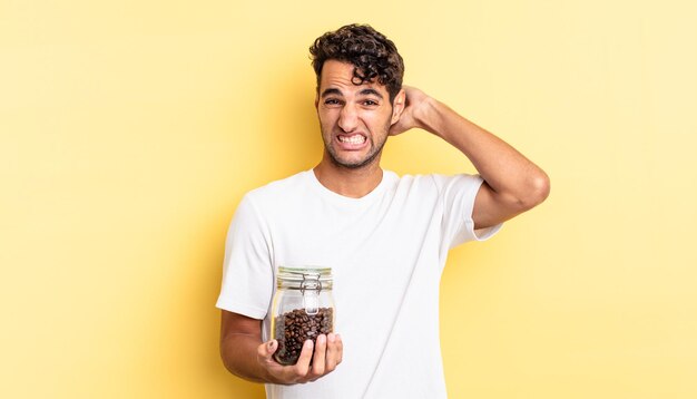 Bel homme hispanique se sentant stressé, anxieux ou effrayé, les mains sur la tête. bouteille de grains de café