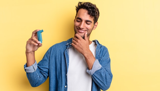 Bel homme hispanique souriant avec une expression heureuse et confiante avec la main sur le menton. notion d'asthme