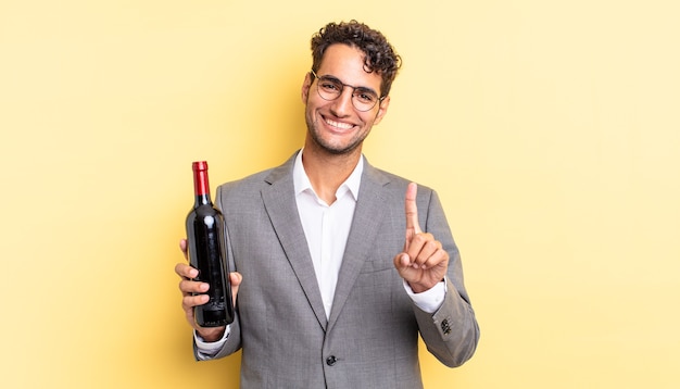 Bel homme hispanique souriant fièrement et en toute confiance faisant numéro un. concept de bouteille de vin