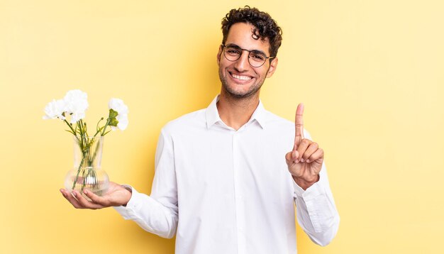 Bel homme hispanique souriant fièrement et en toute confiance faisant numéro un. concept de pot de fleurs