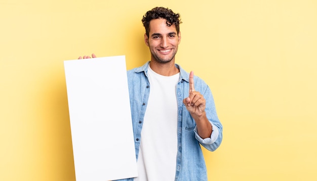 Bel homme hispanique souriant fièrement et en toute confiance faisant numéro un. concept de toile vide