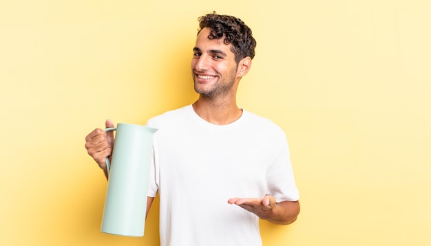 Bel homme hispanique souriant joyeusement, se sentant heureux et montrant un concept. concept de thermos à café