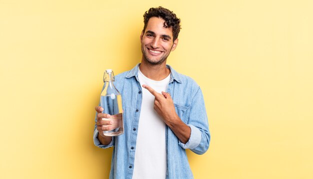 bel homme hispanique souriant joyeusement, se sentant heureux et pointant sur le côté. concept de bouteille d'eau