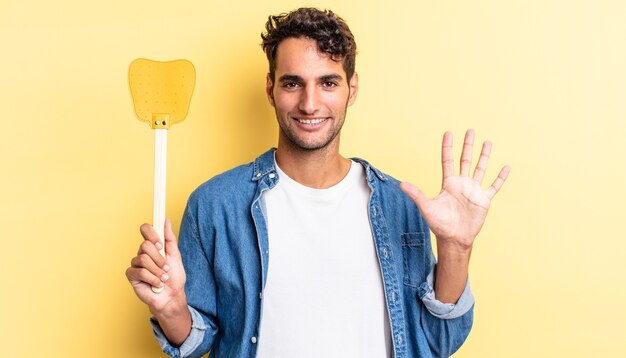 Bel homme hispanique souriant et semblant amical, montrant le numéro cinq. tue le concept de mouches