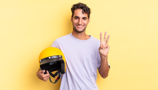 Bel homme hispanique souriant et semblant amical, montrant le numéro trois. concept de casque de moto