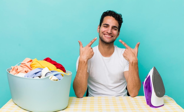 Bel homme hispanique souriant en toute confiance pointant vers son propre concept de fer et de vêtements à large sourire