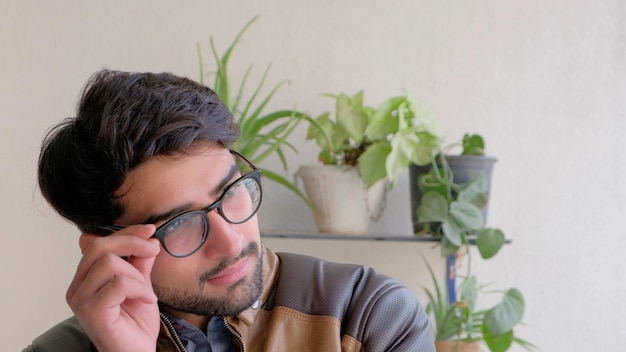 Bel homme indien tenant des lunettes contre un mur avec des plantes en pots