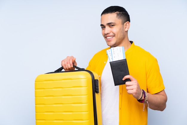 Bel homme isolé sur mur bleu en vacances avec valise et passeport