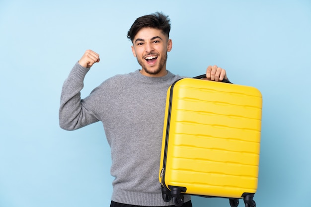 Bel homme isolé sur mur bleu en vacances avec valise de voyage