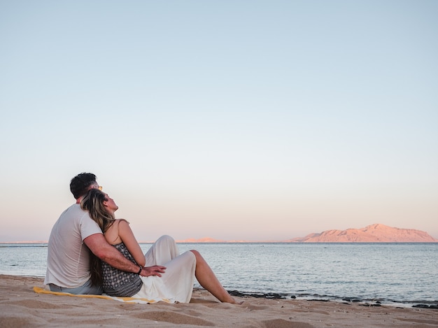 Bel homme et jolie femme assise sur la plage