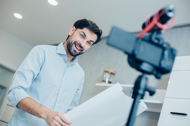 Bel homme joyeux travaillant à domicile et souriant à une caméra tout en tenant une charte graphique