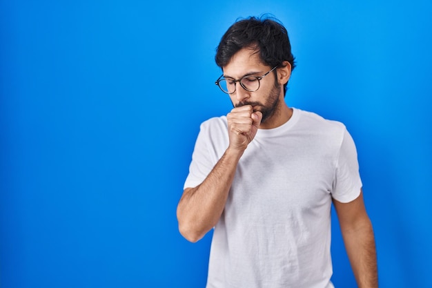 Bel homme latin debout sur fond bleu se sentant mal et toussant comme symptôme de rhume ou de bronchite. notion de soins de santé.