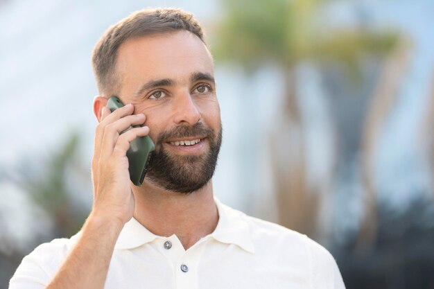 Bel homme latin souriant parlant sur un téléphone portable dans la rue, regardant ailleurs. Copier l'espace