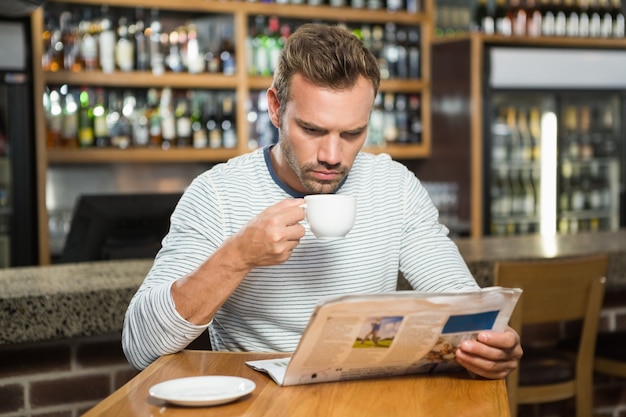 Bel homme lisant un journal et prenant un café