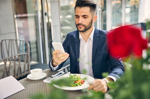 Bel homme lisant un message avant de manger de la salade avant d'aller à la conférence