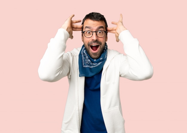 Bel homme avec des lunettes avec une expression faciale surprise et choquée sur fond rose isolé