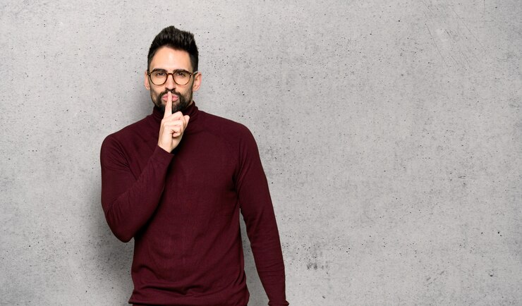 Photo bel homme avec des lunettes montrant un geste du silence mettant le doigt dans la bouche