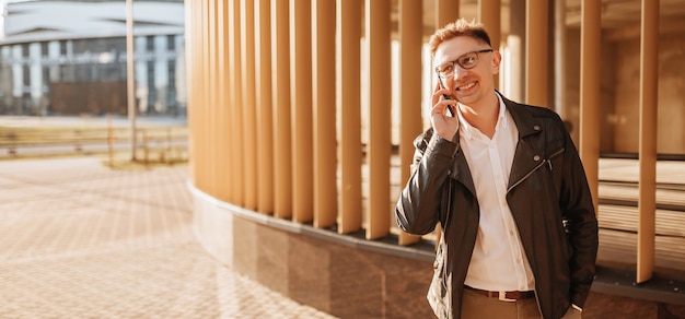 Bel homme avec des lunettes avec un smartphone dans la rue d'une grande ville. Homme d'affaires parlant au téléphone sur fond urbain