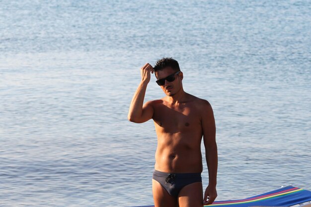 Bel homme avec des lunettes de soleil et maillot de bain profitent de la plage au coucher du soleil Pouilles Salento Italie