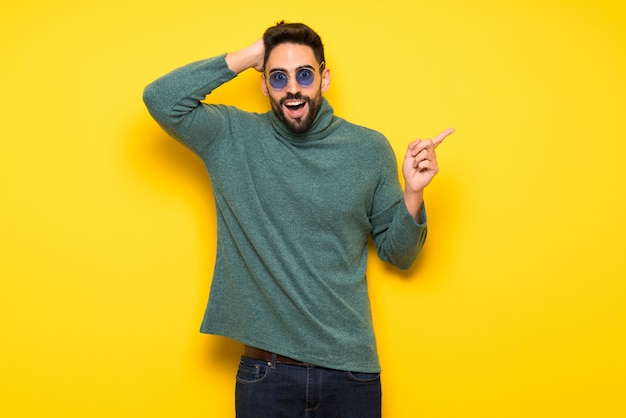 Bel homme avec des lunettes de soleil pointant le doigt sur le côté et présentant un produit