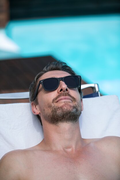 Bel homme à lunettes de soleil se détendre sur une chaise longue