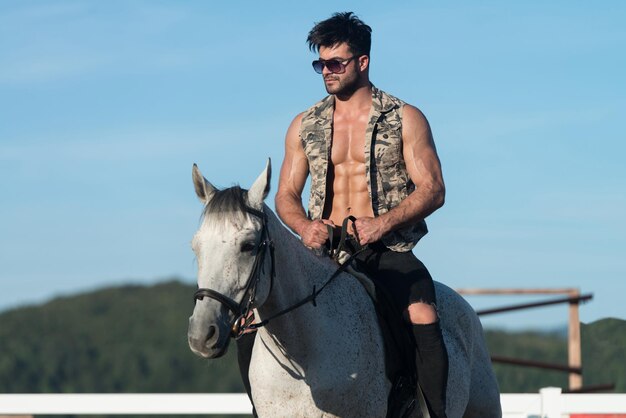 Bel homme macho cowboy à cheval sur un cheval fond de ciel et de montagnes