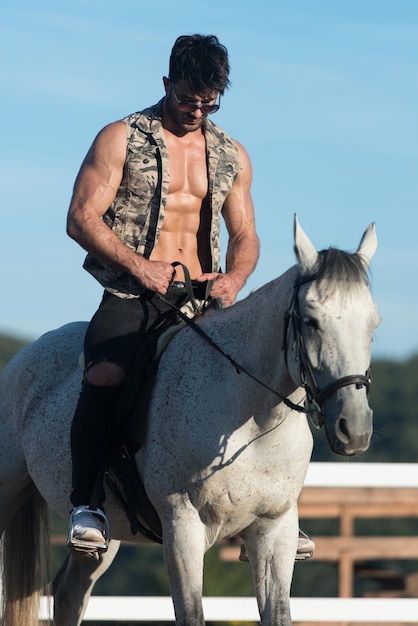 Bel homme macho cowboy à cheval sur un cheval fond de ciel et de montagnes