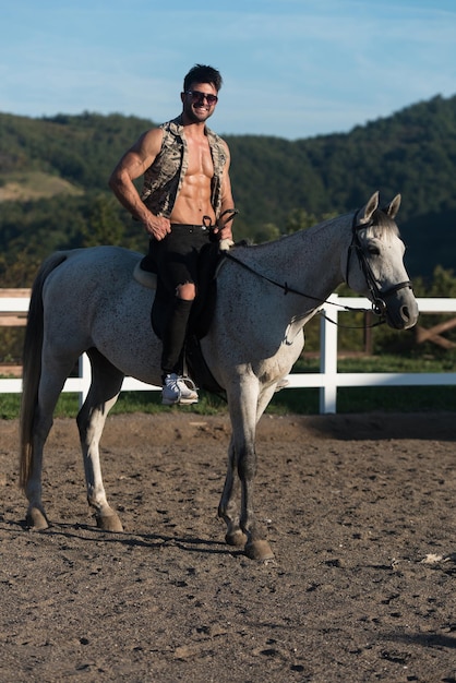 Bel homme macho cowboy à cheval sur un cheval fond de ciel et de montagnes