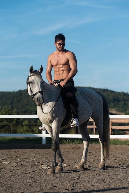 Photo bel homme macho cowboy à cheval sur un cheval fond de ciel et de montagnes