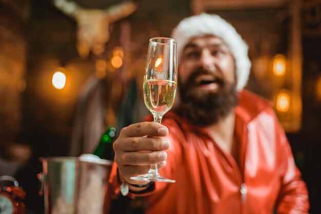 Bel homme macho portant des vêtements de père Noël homme avec barbe tient une coupe de champagne vacances