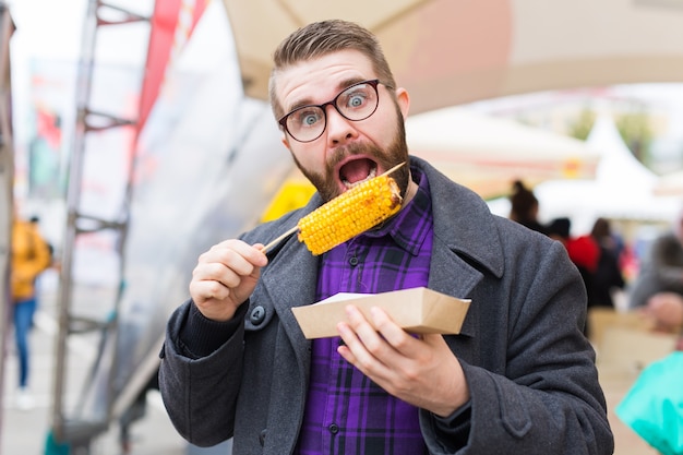 Bel homme mangeant du maïs grillé dans la rue.