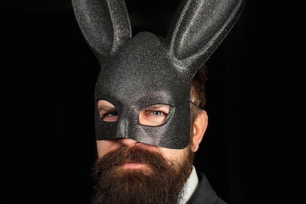 Bel homme en masque de carnaval lapin de salle de bal avec de longues oreilles sensuelles sur fond noir Homme sérieux avec barbe en masque de rabit