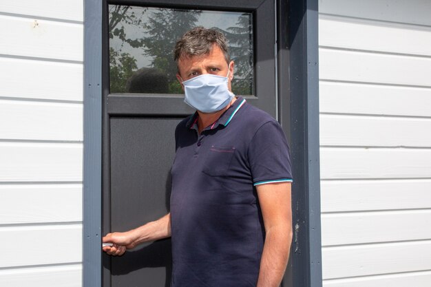 Bel homme avec un masque de protection avant la porte de la maison confinée en quarantaine pendant l'épidémie de coronavirus Covid-19