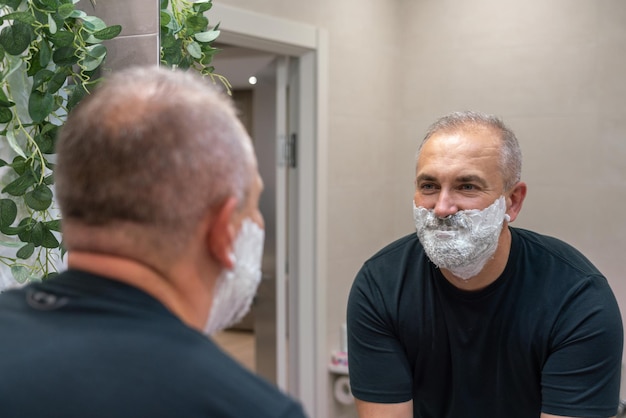 Bel homme mature appliquant de la mousse à raser sur son visage pour couper sa barbe et sa moustache avec un rasoir