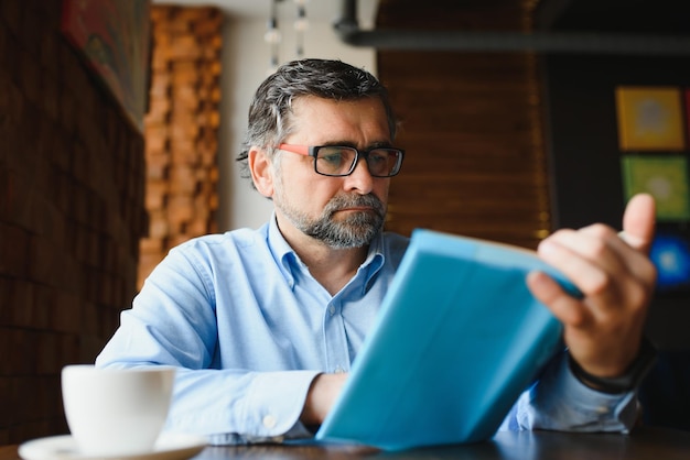 Bel homme mature lisant un livre dans un café